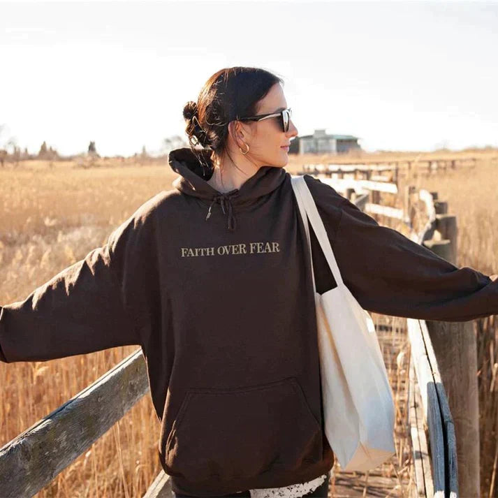 Frau in braunem "Faith Over Fear" Hoodie, Baumwolle, Unisex, Herbstmode, Naturhintergrund.