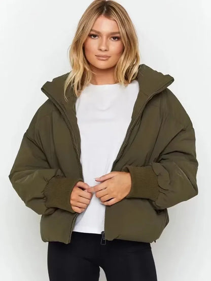 Frau trägt olivgrüne Daunenjacke, weißes T-Shirt, schwarze Hose. Wintermode, Damenbekleidung.