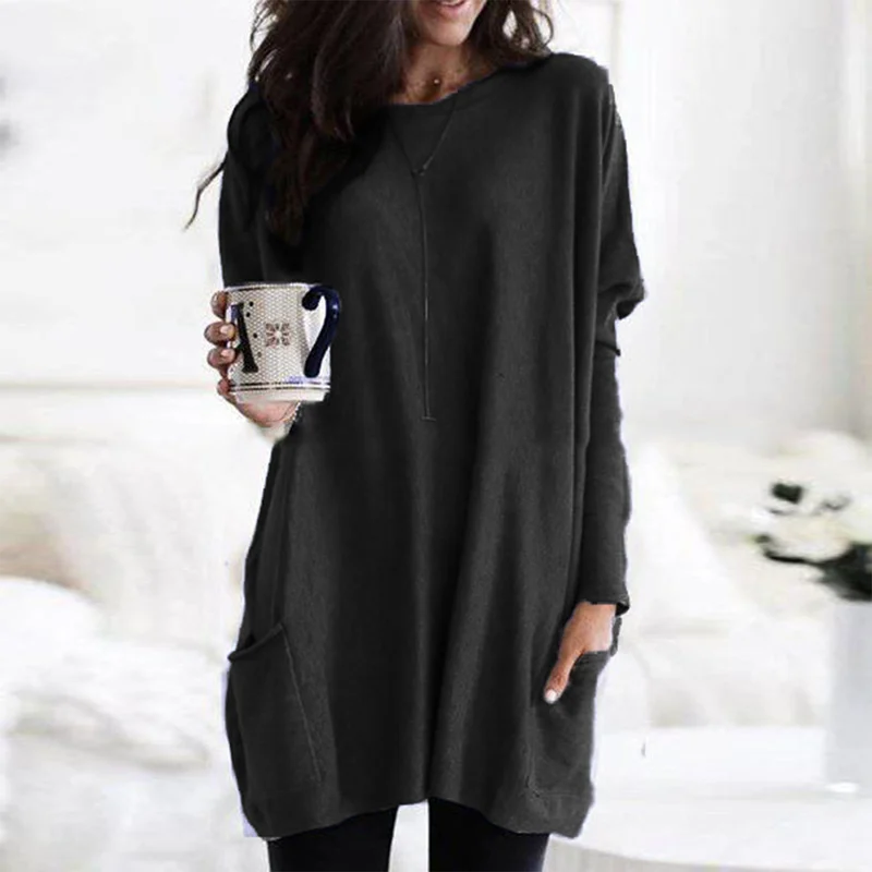 Frau in schwarzem Oversize-Pullover mit Kaffeetasse, gemütliche Wintermode, Wohnzimmer.