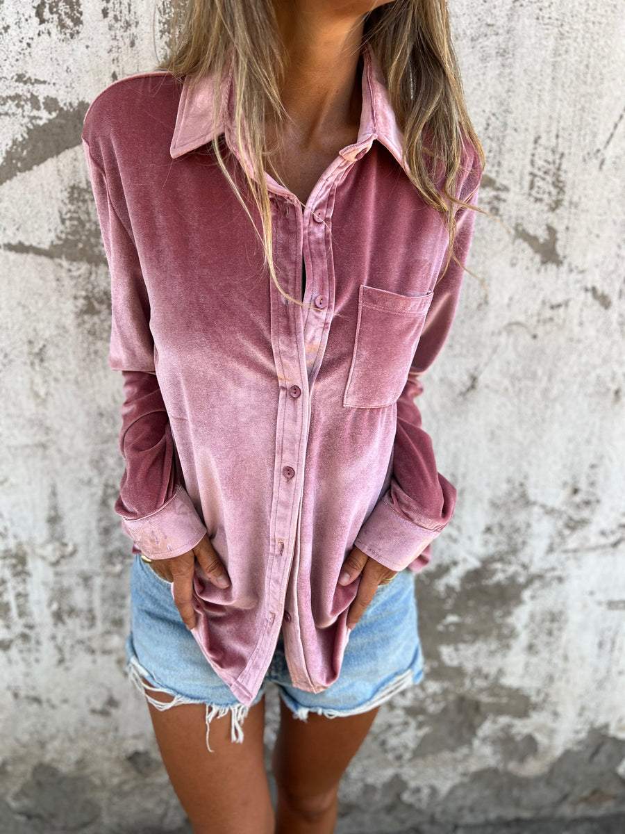 Frau in rosa Samthemd und Jeansshorts vor Betonwand.