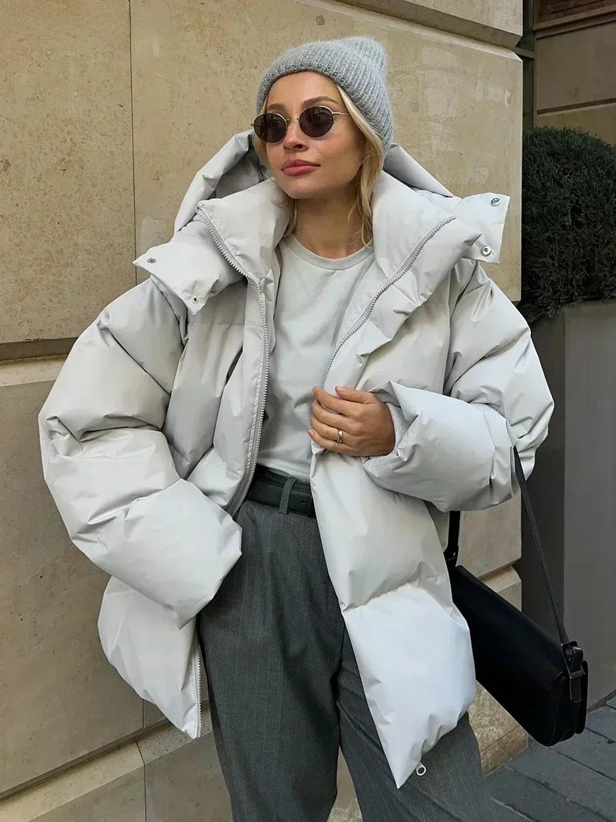 Frau in grauem Daunenmantel, grauer Mütze, Sonnenbrille, lässiger Wintermode-Look.