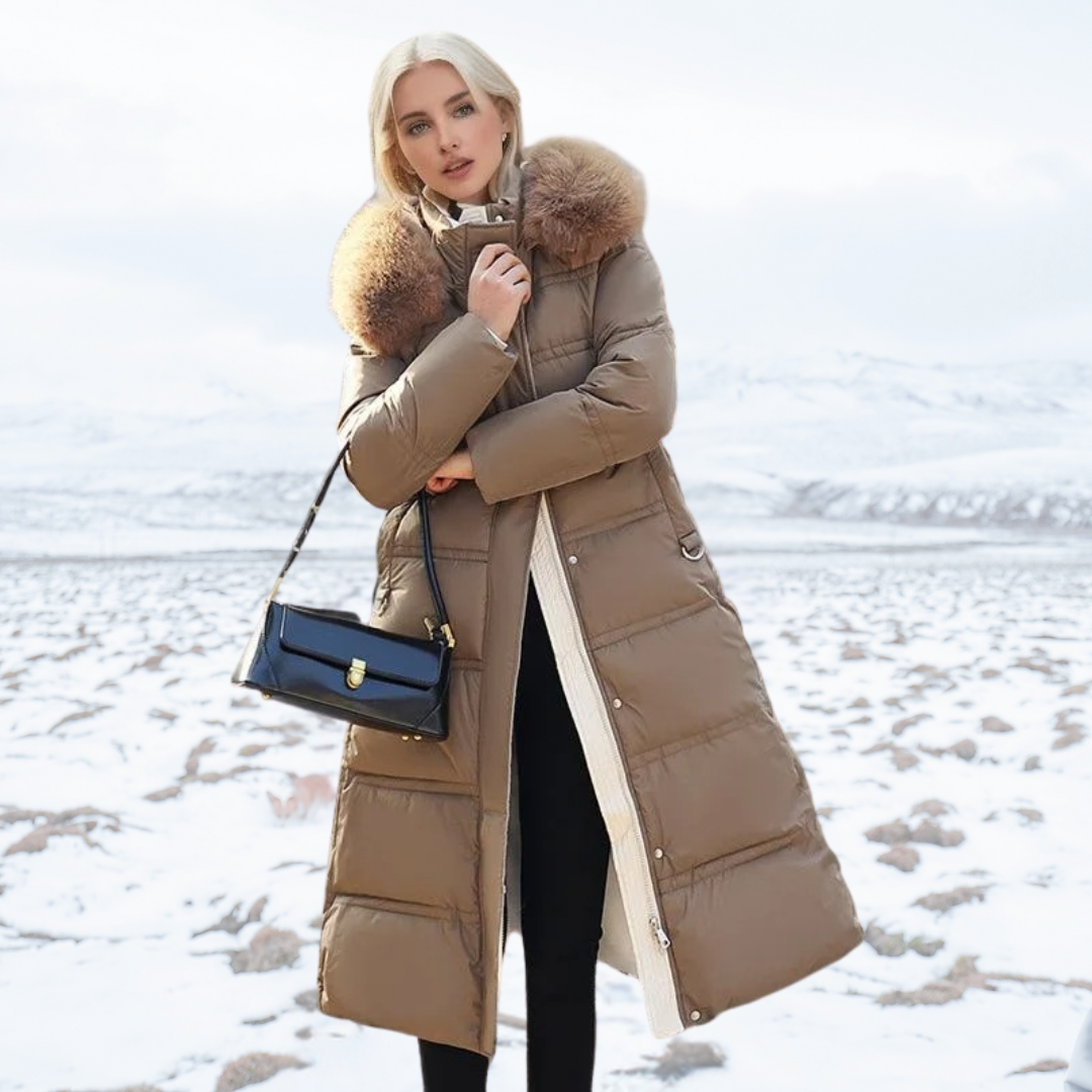 Frau in braunem Daunenmantel mit Pelzkragen, schwarze Handtasche, schneebedeckte Landschaft.