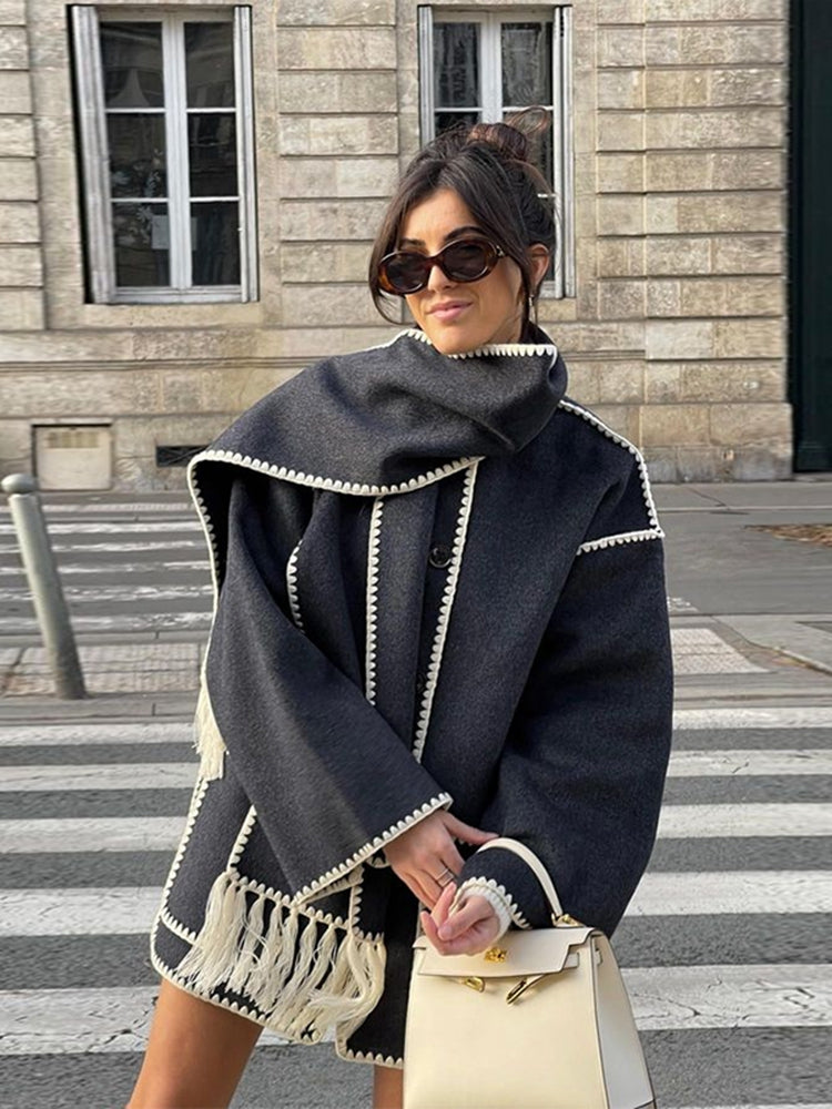 Frau in schwarzem Mantel mit Fransen, Sonnenbrille und Handtasche auf Zebrastreifen.