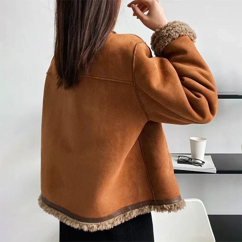 Rückansicht der braunen Jacke mit Lammfellsaum am unteren Rand und am Ärmel, Model hebt die Hand 3