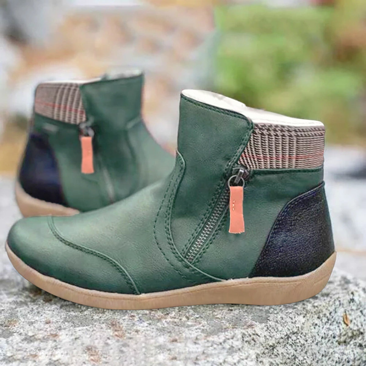 Grüne Stiefeletten mit seitlichem Reißverschluss, kariertem Schaftrand und dunkler Fersenkappe, auf einem Stein im Freien.