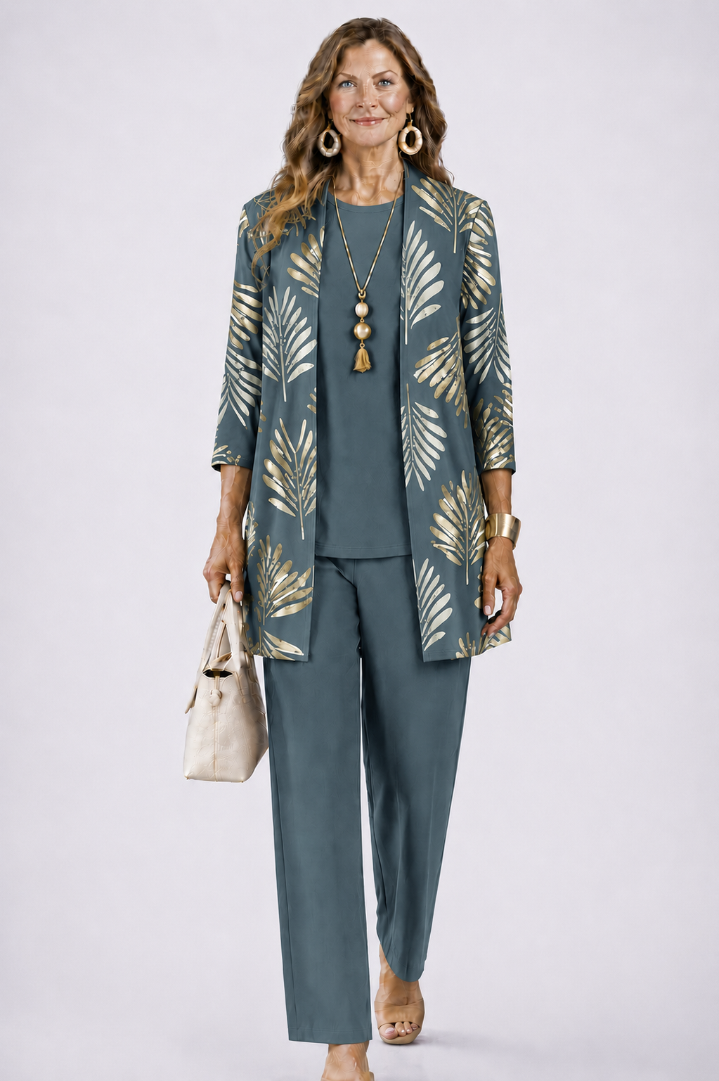 Frau im graublauen Set mit goldenem Palmblattmuster auf dem offenen Cardigan, dazu Rundhalsshirt, weite Hose und cremefarbene Handtasche. 1