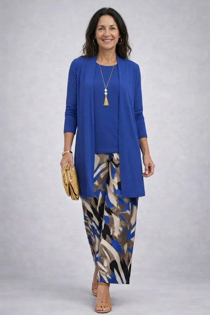 Frau im königsblauen Set aus langem Cardigan und Shirt, kombiniert mit weiter Hose in blau-braun-beigem Abstraktmuster, goldene Clutch. 9