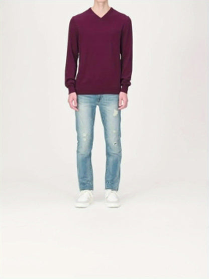Person in burgunderrotem V-Ausschnitt-Pullover, hellblauer Jeans und weißen Sneakers.