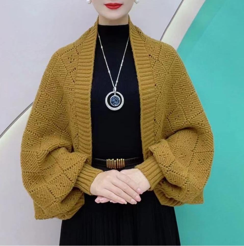 Senfgelbe Strickjacke mit Ajourmuster, getragen zu schwarzem Oberteil und Rock vor türkisfarbener Wand 1
