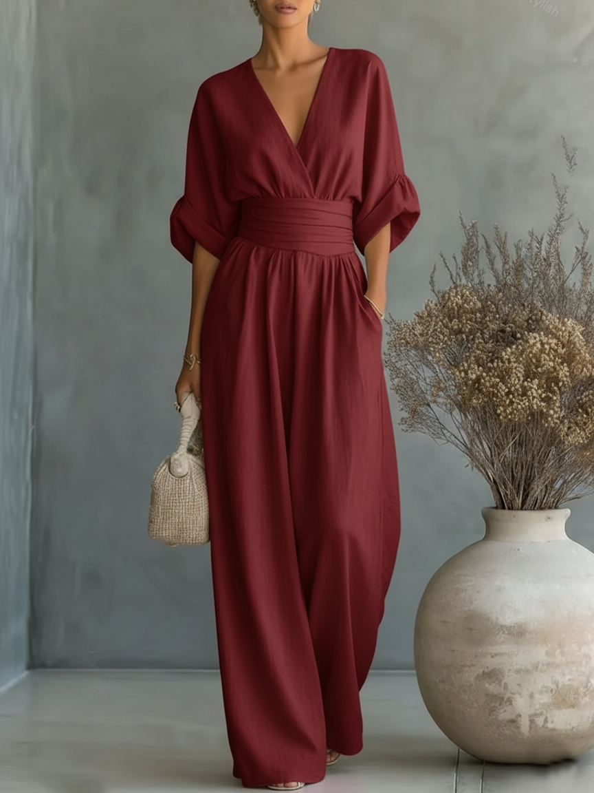 Model im weinroten Jumpsuit mit weiten Fledermausärmeln, hoher Taille und fließendem Hosenbein vor grauer Wand 3
