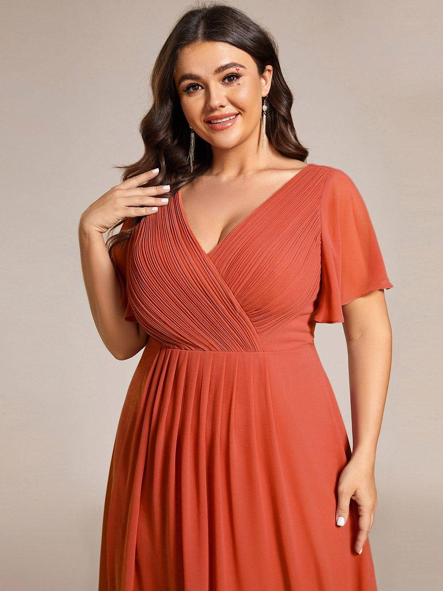 Nahaufnahme des terrakottafarbenen Oberteils an einem Plus-Size-Model mit plissiertem V-Ausschnitt und Flatterärmeln, eine Hand an der Schulter. 99