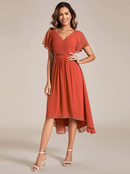 Model in terrakottaorangem Chiffonkleid mit plissiertem V-Ausschnitt, Flatterärmeln und Hoch-Tief-Saum, Hand an der HĂĽfte, weiĂźe Sandaletten. 92