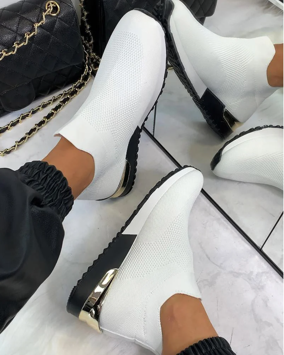 Weiße elastische Damen-Sneaker, atmungsaktiv, mit goldenen Akzenten, auf Marmorboden.