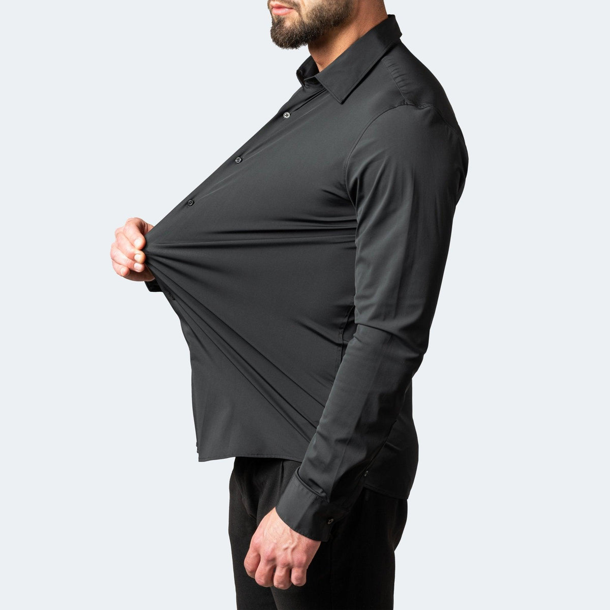 Schwarzes Herren-Stretchhemd in Seitenansicht, der Stoff wird vor dem Bauch weit nach vorn gezogen.