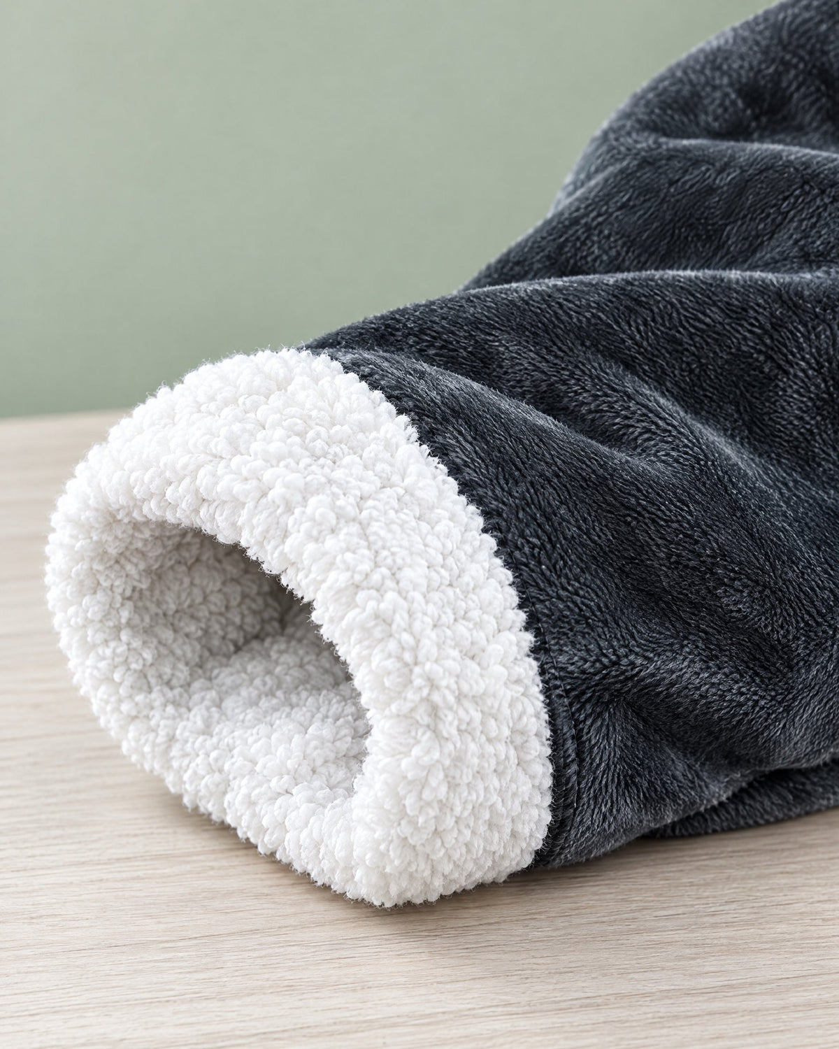 Detailaufnahme eines Ärmelaufschlags mit weißem, lockigem Plüschfutter und dem weichen grauen Außenstoff auf einer Holzfläche. 8