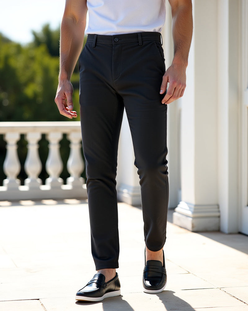 Dunkle Chino in einer weiteren Ansicht auf einer Terrasse mit weißem Shirt und schwarzen Lederslippern mit weißer Sohle.
