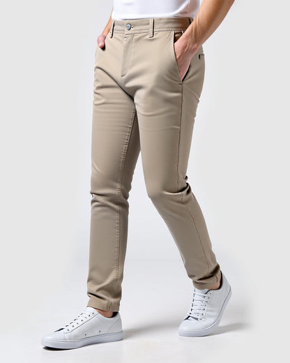 Beige Chino seitlich von vorn mit weißem Shirt und weißen Sneakern vor hellem Hintergrund.