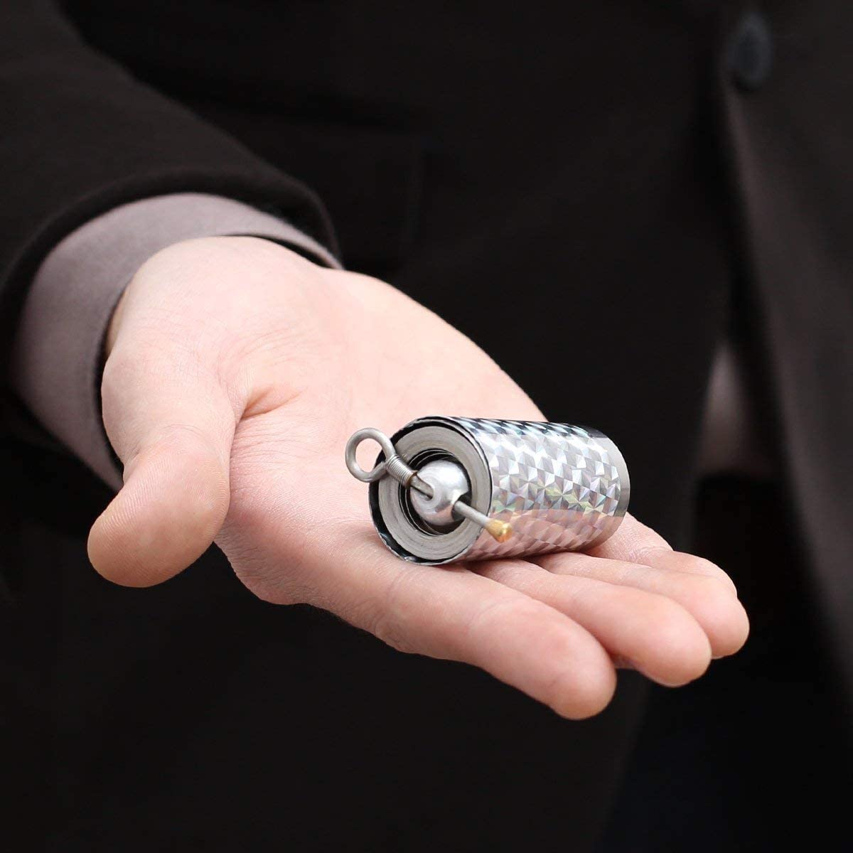 Der zusammengerollte Stab liegt als kleine Metallrolle mit Ring und Messingknopf auf einer offenen Handfläche 1