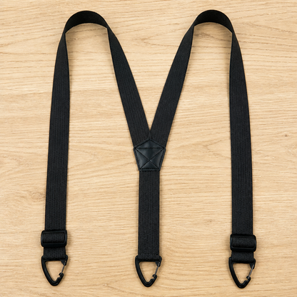 Schwarze Y-Hosenträger mit Verstellern nahe den Clips und kleinem Lederkreuz, flach auf hellem Holz ausgebreitet. 13