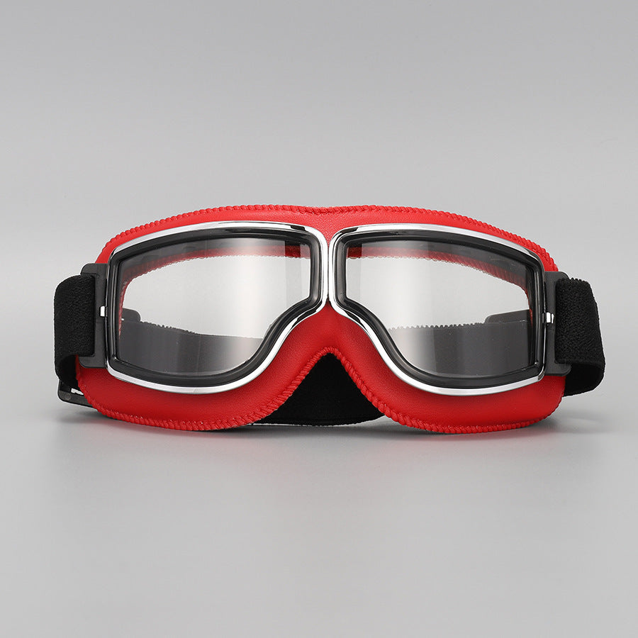 Brille mit rotem Lederrand, Chromrahmen und klaren Gläsern, seitlich gepolsterte schwarze Riemenenden, auf grauem Hintergrund. 10