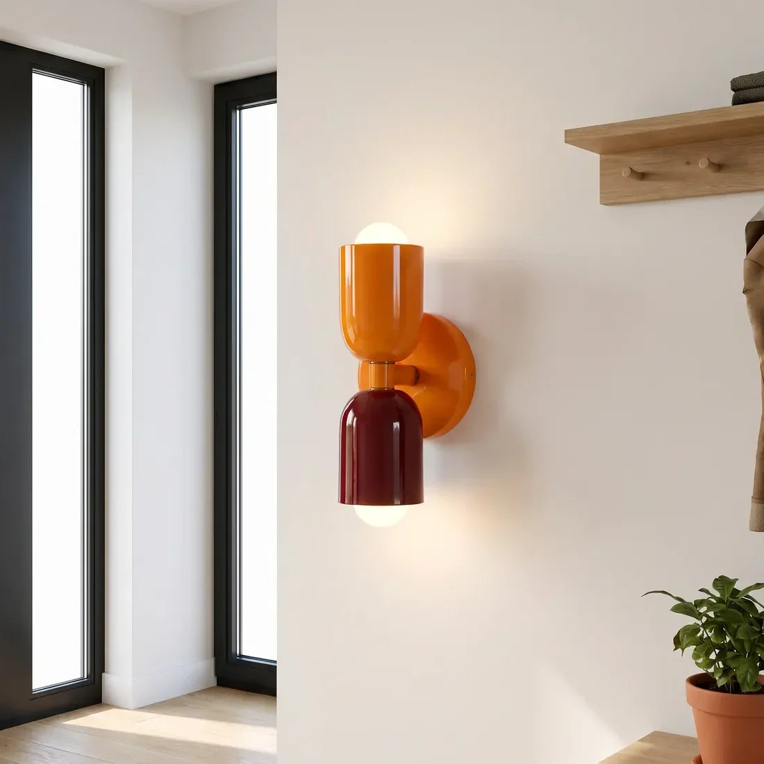 Wandlampe in Orange und Burgunderrot neben hohen Fenstern im Eingangsbereich, mit Holz-Garderobenleiste und Topfpflanze. 11