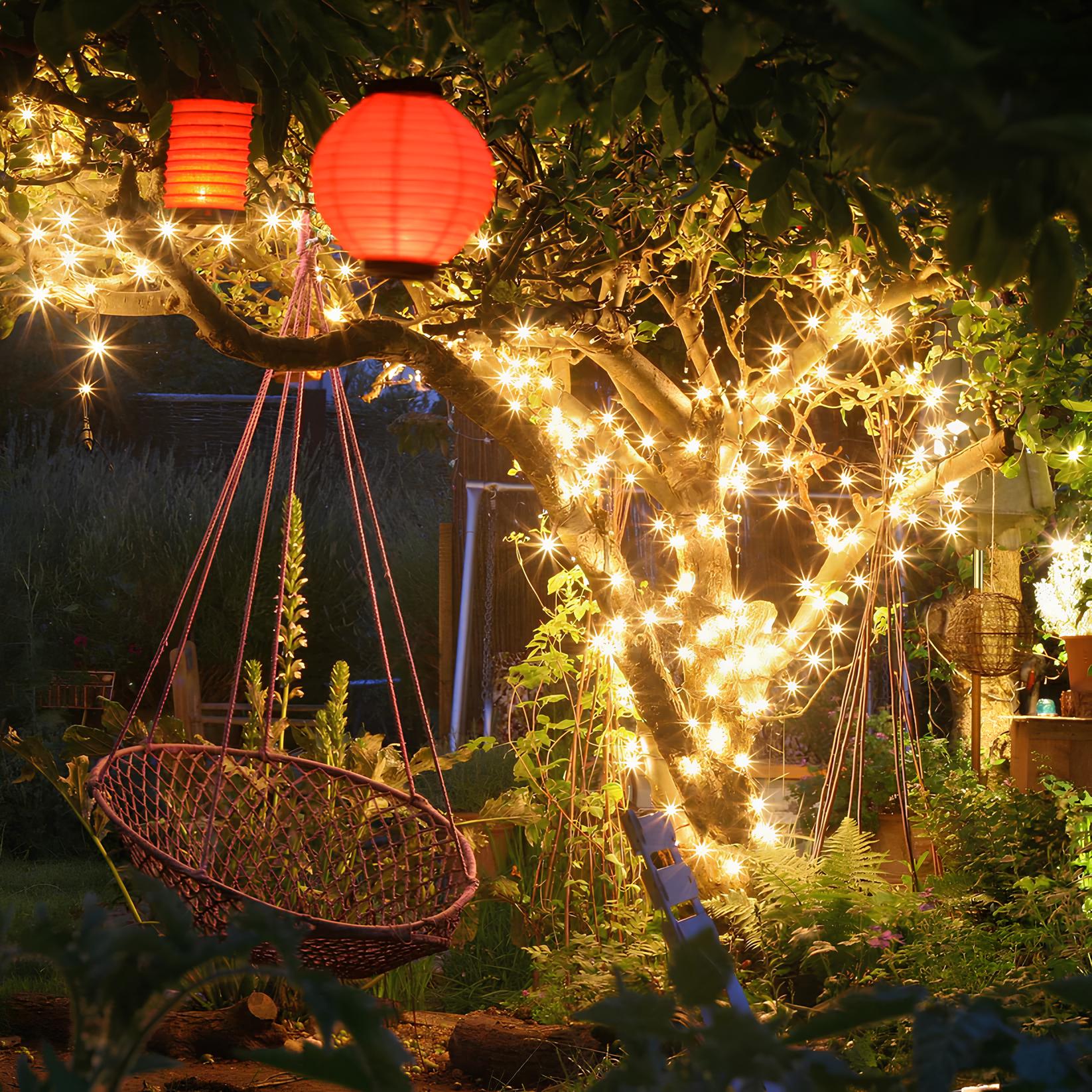 Garten mit Lichterketten, roter Papierlaterne und Hängesessel bei Nacht, stimmungsvolle Beleuchtung.