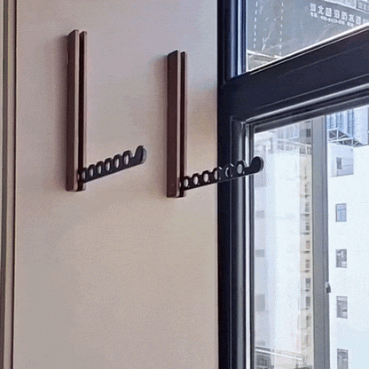 Zwei dunkle Holz-Wandhaken mit ausgeklapptem schwarzem Arm an einer hellen Wand neben einem Fenster. 2