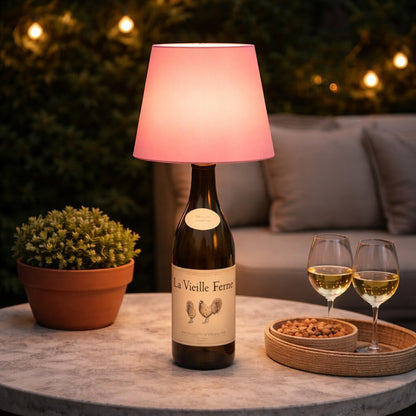 Rosa leuchtende Flaschenlampe auf Weinflasche, auf Gartentisch mit Pflanze, zwei Weingläsern und Nüssen 19