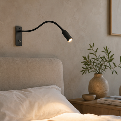Schwarze Wandlampe leuchtet warm über einem Bett mit Leinenkopfteil