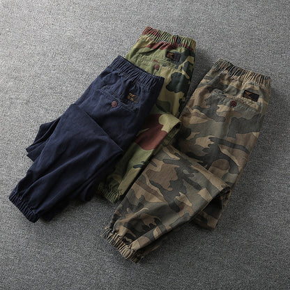 Drei Herren-Cargohosen, Camouflage und Blau, elastischer Bund, auf grauem Hintergrund.
