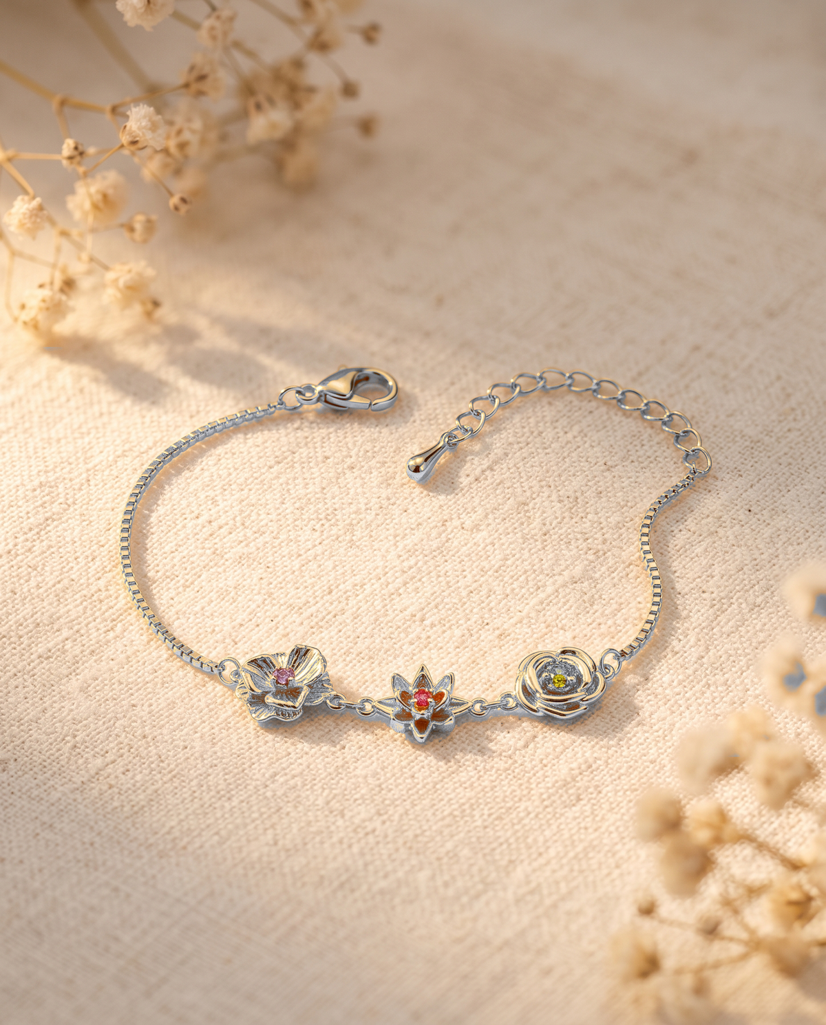 Silberfarbenes Blumenarmband mit Verlängerungskette auf Leinenstoff, umgeben von getrockneten Blütenzweigen. 13