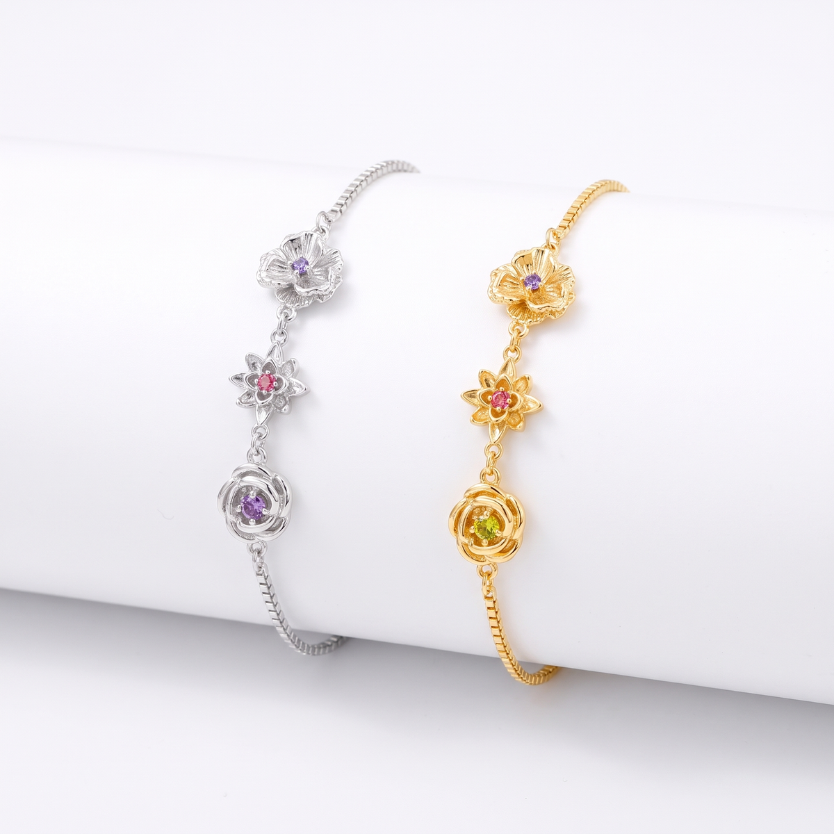 Zwei Armbänder nebeneinander, eines in Silber und eines in Gold, jeweils mit drei Blumen und Steinen. 3
