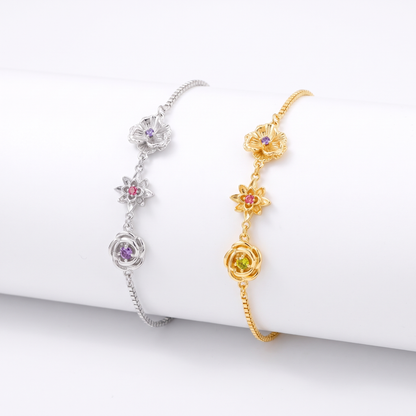 Zwei Armbänder nebeneinander, eines in Silber und eines in Gold, jeweils mit drei Blumen und Steinen. 3