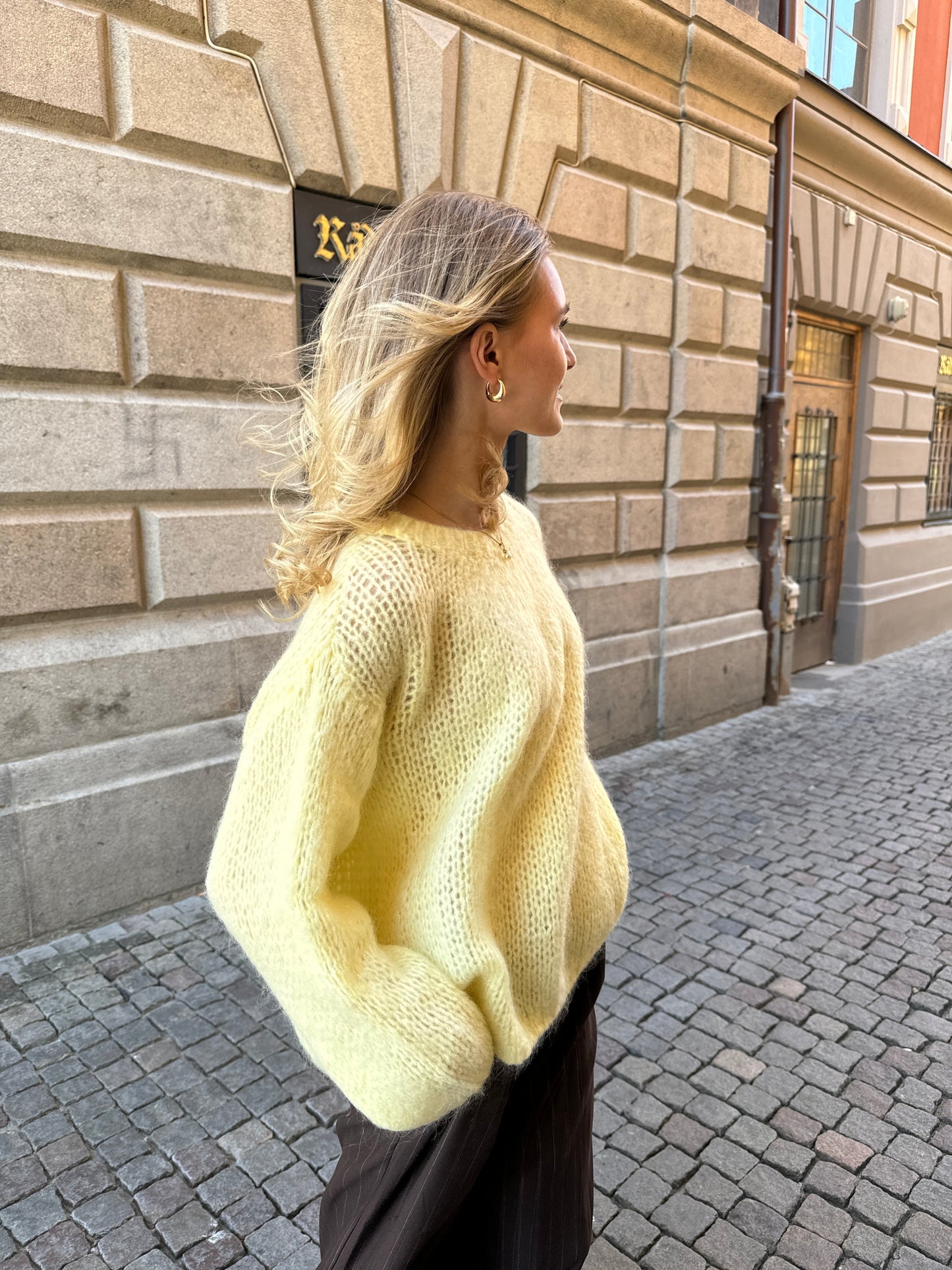 Frau in gelbem Strickpullover auf Kopfsteinpflasterstraße, modisch, Herbstmode, Stadt.
