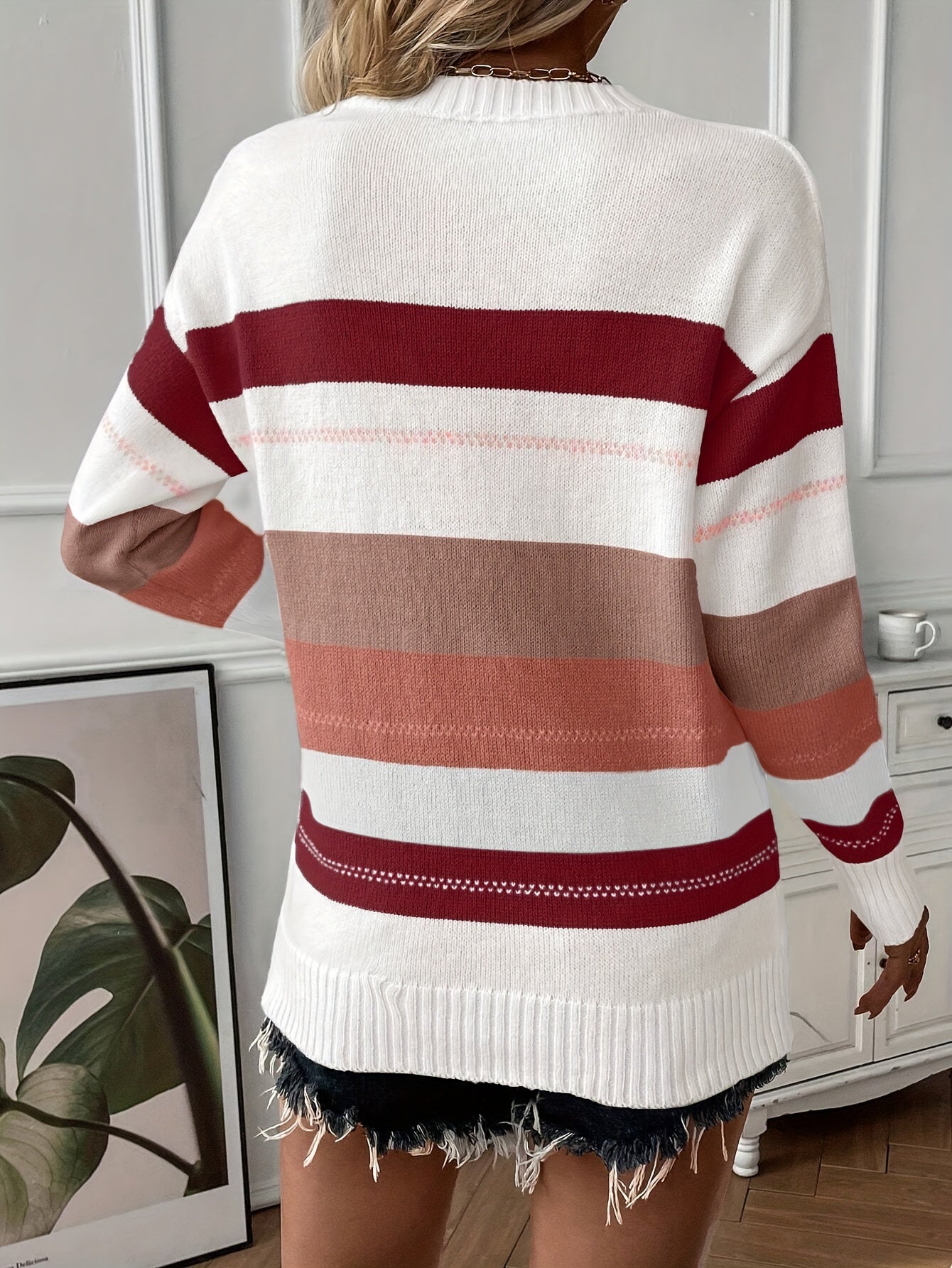 Frau in gestreiftem Pullover, rot-weiß-braun, vor Wand mit Pflanzenbild, modisch, lässig.