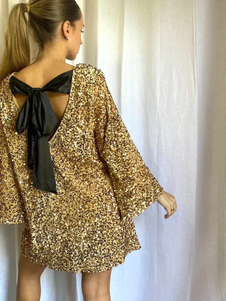 Frau in goldenen Pailletten-Kleid mit langen Ärmeln und schwarzer Schleife, festliche Mode.