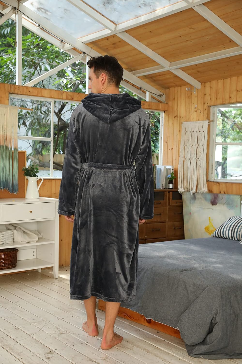 Mann im grauen Fleece-Bademantel mit Kapuze im Schlafzimmer, gemütlich und warm.