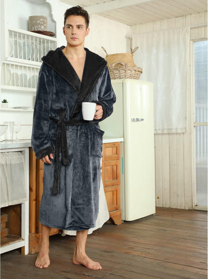 Mann im grauen Fleece-Bademantel mit Kapuze, hält Tasse, steht in rustikaler Küche.
