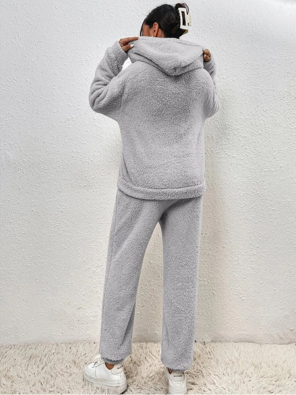 Frau in grauem Fleece-Hoodie und Jogginghose, gemütliche Wintermode, Rückansicht.