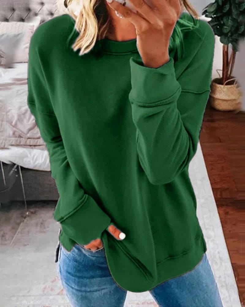 Frau in grünem Pullover und blauer Jeans, gemütliches Wohnzimmer, modische Freizeitkleidung.