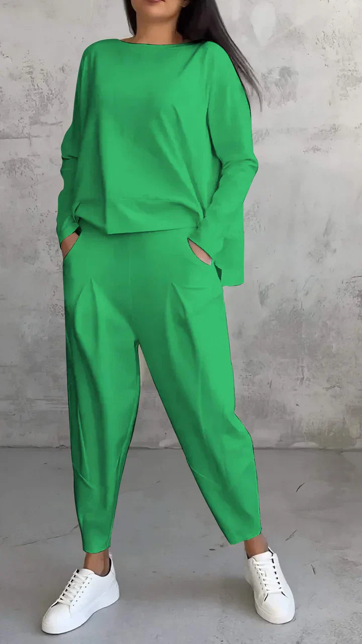 Frau in grünem Oversize-Sweatshirt und Jogginghose, weiße Sneaker, grauer Hintergrund.