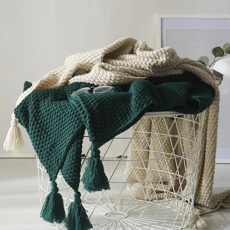 Grüner Strickplaid mit Quasten auf weißem Drahtkorb, dekorativer Wohnaccessoire.