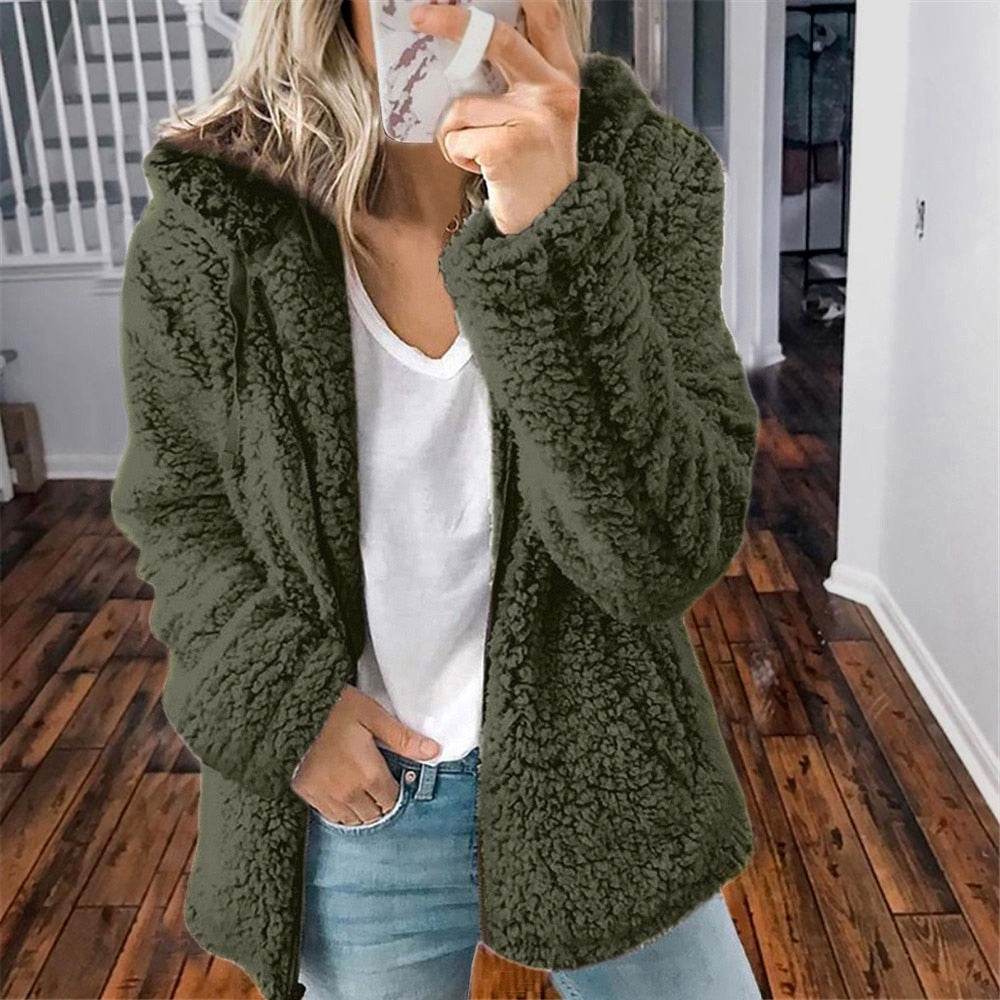 Frau in grüner Teddyjacke, weißem T-Shirt und Jeans in modernem Innenraum.