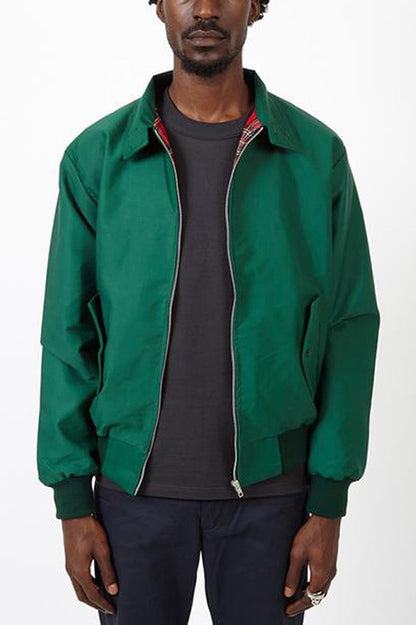 Mann trägt grüne Harrington-Jacke, schwarzes T-Shirt, dunkle Hose.