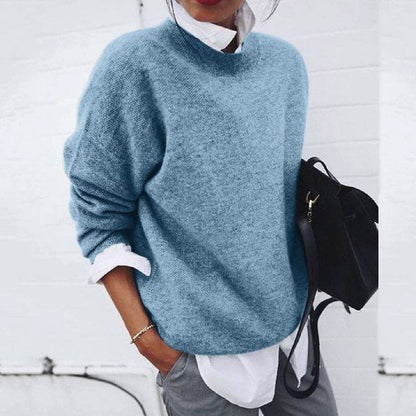 Frau in blauem Strickpullover, weißer Bluse, grauer Hose, schwarze Tasche, lässiger Stil.
