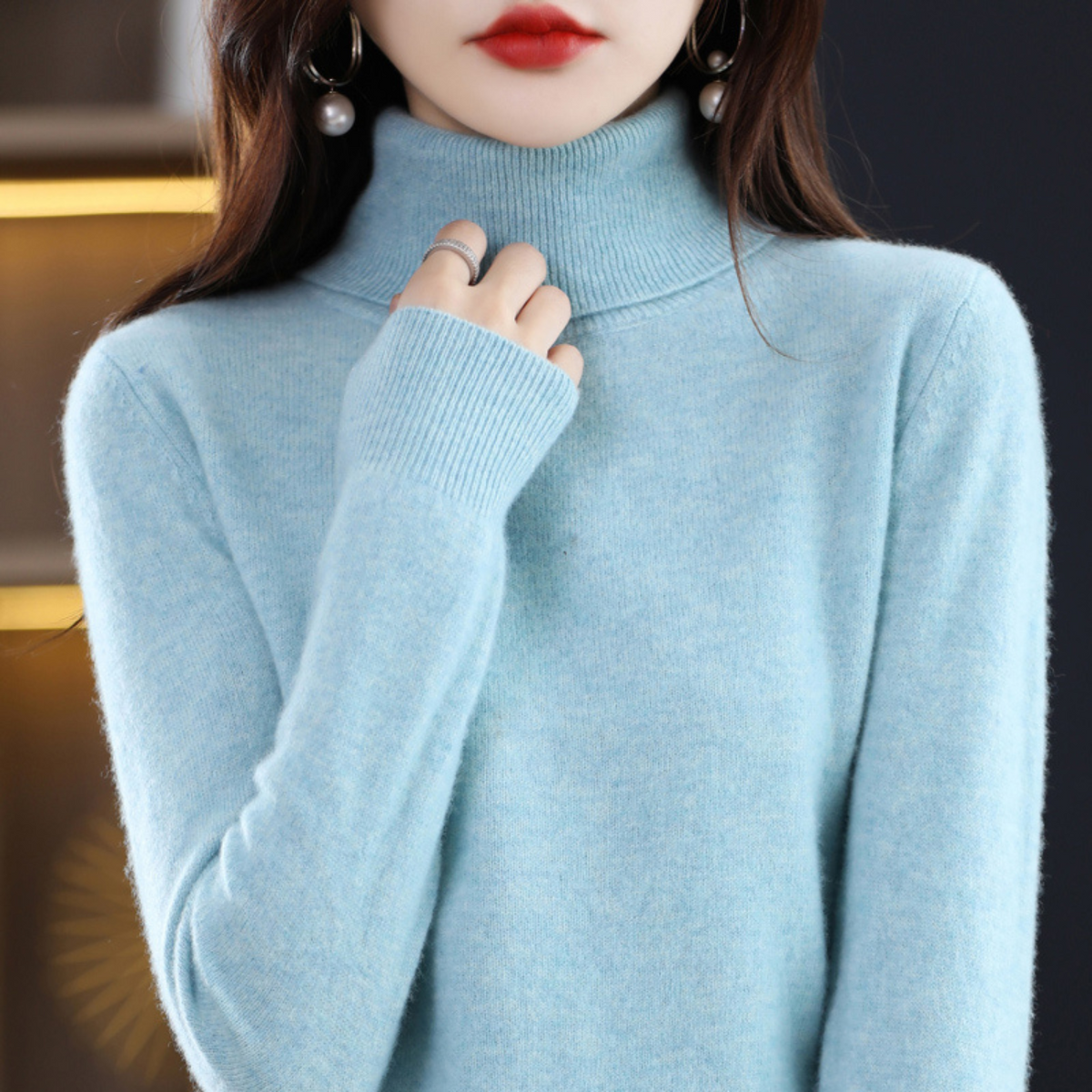 Hellblauer, meliert wirkender Rollkragenpullover am Model mit gerippten Ärmelbündchen.