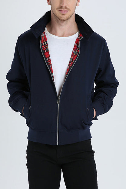 Mann in dunkelblauer Harrington-Jacke mit rotem Karofutter, weißem T-Shirt und schwarzer Hose.