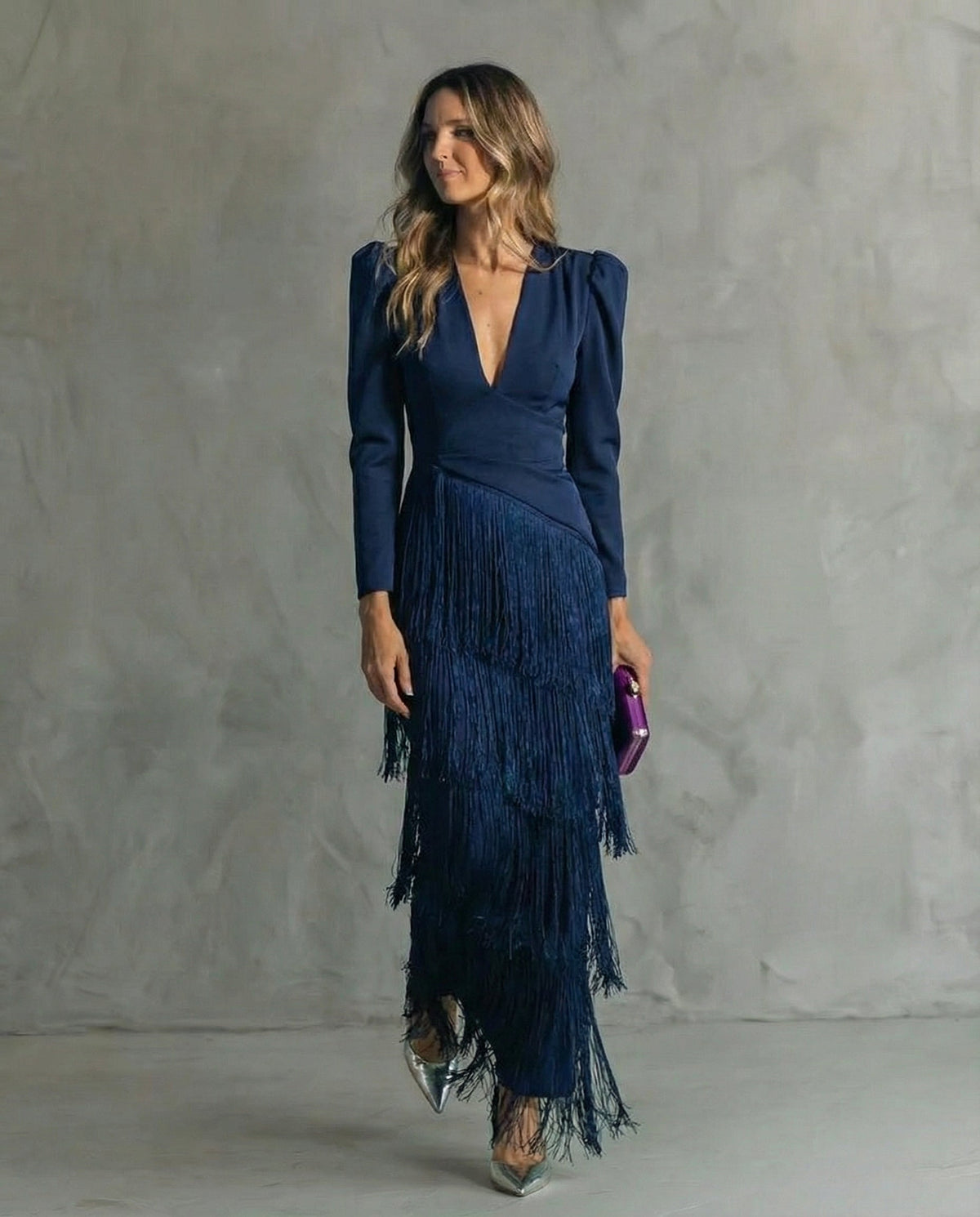 Frau im marineblauen Kleid mit V-Ausschnitt und mehrlagigen Fransen, lila Clutch in der Hand 6