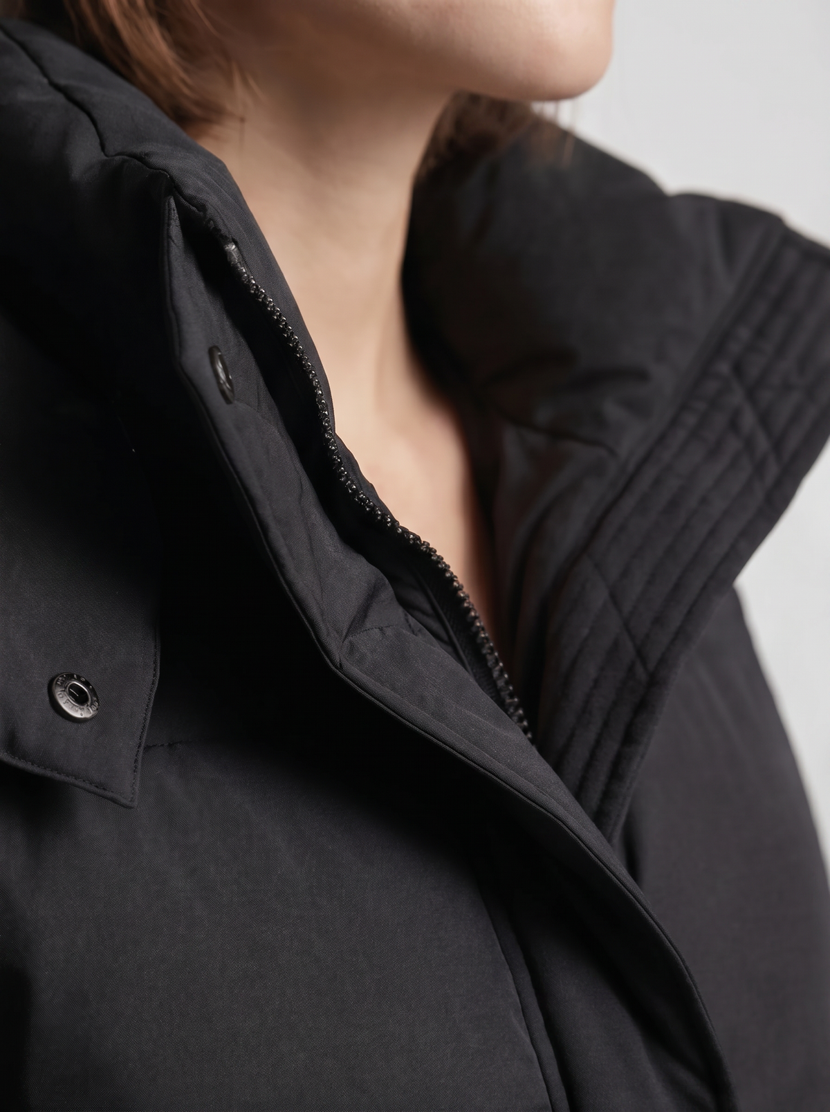 Nahaufnahme von Stehkragen, Reißverschluss, Druckknopf und Steppnähten der schwarzen Jacke am Model 7