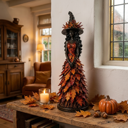 Hexenfigur in rotem Blätterkleid mit Hut auf rustikalem Holztisch neben Kerze, Kürbis, Eicheln und Herbstlaub in gemütlichem Wohnzimmer. 1